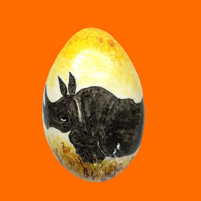Næsehorn malet på gåseæg. Farverne mørke, sorte og gule. Ægget er fortogrsferet på orange baggrund